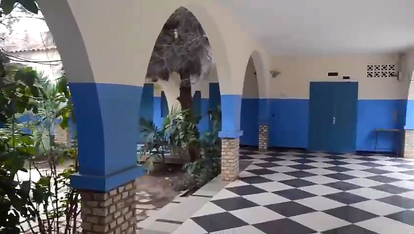 Couloir au sol carrelé en damier, ouvert sur les arcades et les plantes de la cour